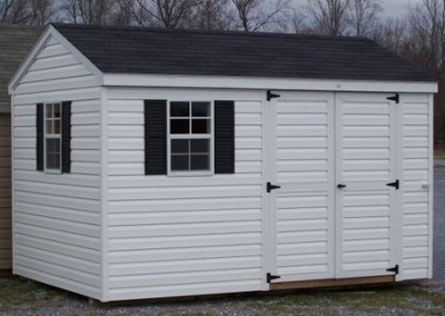 A white vinyl shed with a black shingled, a-roof style roof. Shed is 8x12 and has a double doors and two windows