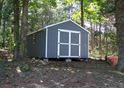A 12x16 painted shed with an a-roof style shingled roof. The shed has two windows and a set of double doors