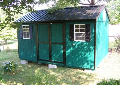 A 10x14 painted shed with black trim. Shed has a black metal, a-roof style roof and a set of double doors as well as two windows with black shutters
