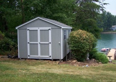A 10x14 grey painted shed with white trim. The shed has a shingled, a-roof style roof, two windows with shutters, and a solid double door