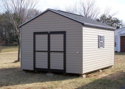A vinyl shed with an a-roof style, shingled roof. Shed has a 6 foot wide double door on gable end and a window on either side of shed