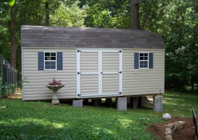 A vinyl shed sized at 12x20. Shed has a barn style, shingle roof and two windows with shutters and a set of solid vinyl double doors