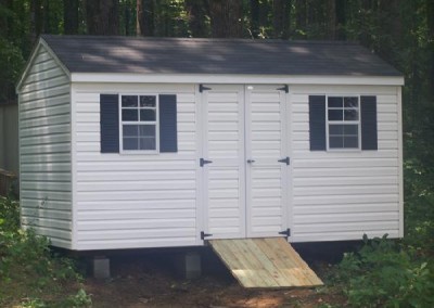 A white vinyl shed sized 8x14 Shed has a shingled, a-roof style roof. The shed has a 4 foot wide double door, two windows and a wooden ramp